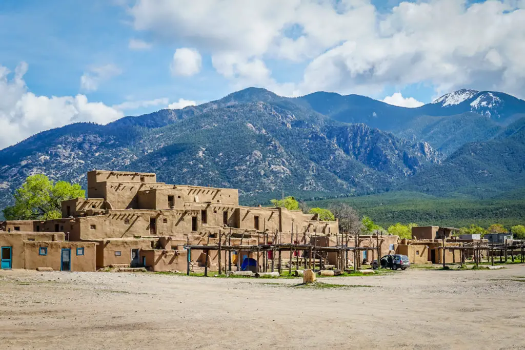 The low adobe buildings of Taos Pueblo backdropped by tree-covered mountains in New Mexico