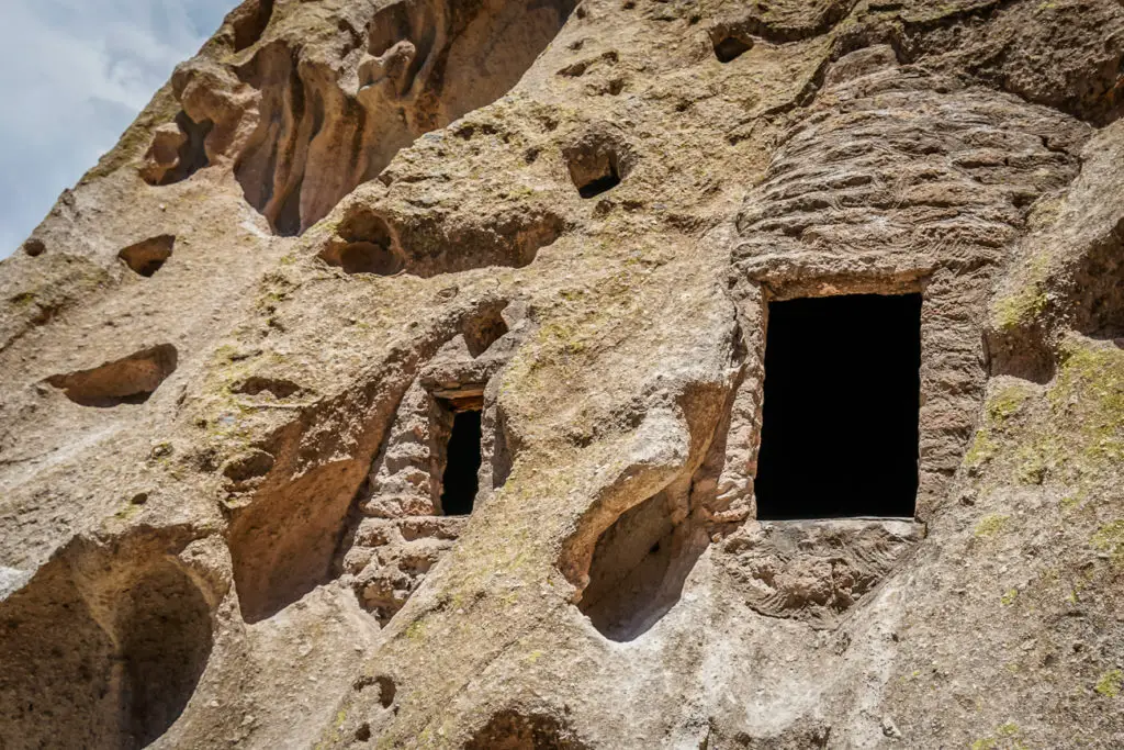 Close-up of ancient cave dwellings at Bandeleir National Monument in New Mexico, with multiple small openings in a cliff face, showing signs of erosion and weathering.