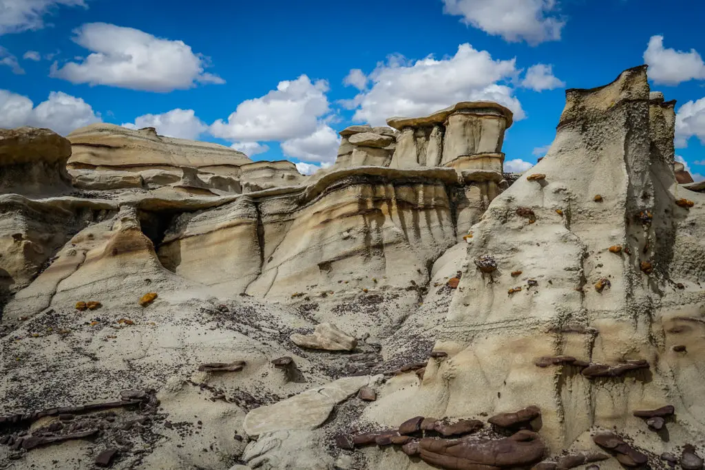 A landscape of unique rock formations with layers of sediment, creating a dramatic and rugged terrain under a partly cloudy sky. This is Bisti Badlands, one of the most interesting places for your New Mexico itinerary.