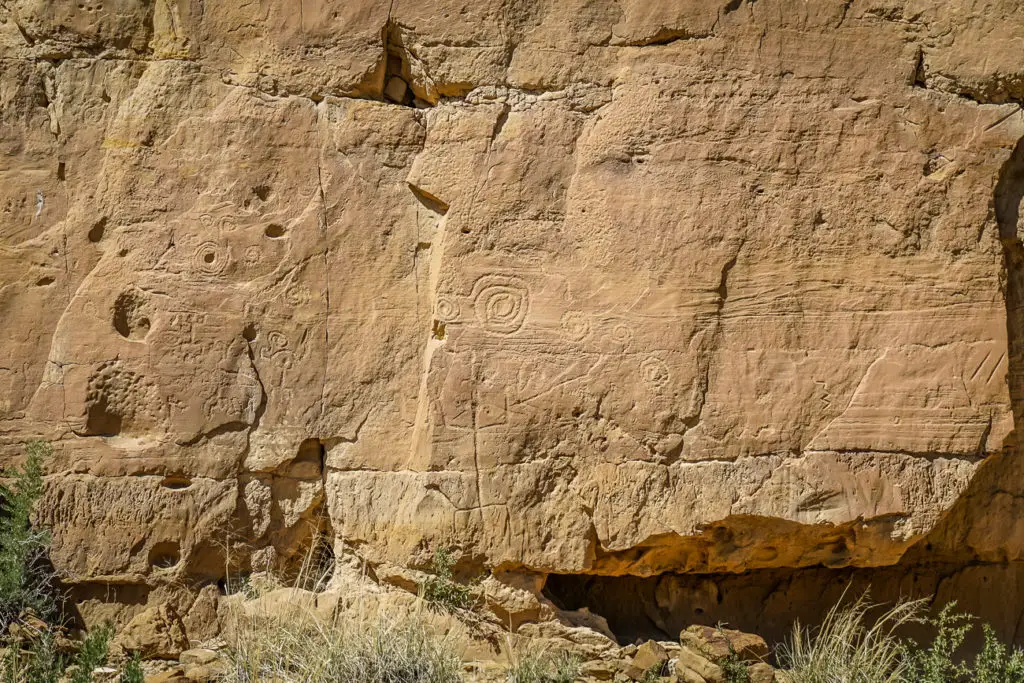 An ancient rock face at Chaco Cultural Natural Historic Park with intricate petroglyphs, showcasing the artistic expression of indigenous peoples from centuries past.