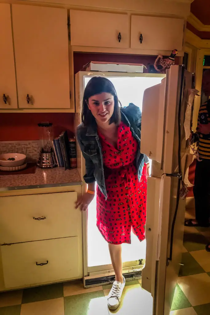 A woman - the author of this article - in a denim jacket and red dress with black hearts stepping through a doorway into a sunlit room, with a friendly expression on her face. This photo was taken at Meow Wolf, one of the coolest things to do in Santa Fe New Mexico.