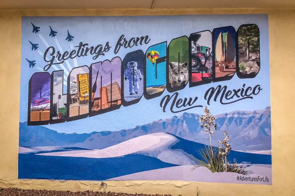 A colorful mural with the message "Greetings from Alamogordo, New Mexico," featuring various images representing the state, including landscapes, wildlife, and cultural icons.