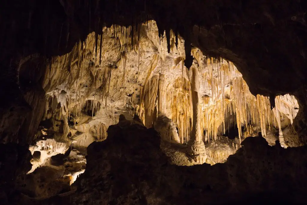 The interior of Carlsbad Cavern showing an array of natural stalactites and stalagmites illuminated against the dark backdrop of the cave. This is one of the best places to visit in New Mexico for people interested in the natural world.