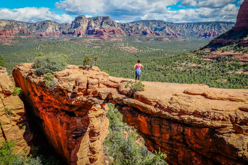 A woman in a pink top stands on top of Devil's Bridge in Sedona, one of the bucket list-worthy hikes