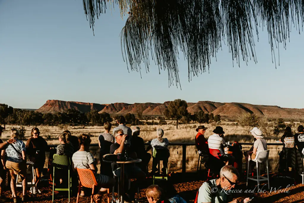 A group of people socialising at an outdoor setting with tables and chairs, enjoying the view of a rugged mountain range in the distance. Kings Canyon Resort is one of the best places to stay near Kings Canyon.