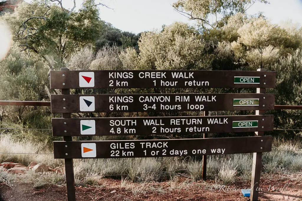 A trail signpost with various walking track options including Kings Creek Walk, Kings Canyon Rim Walk, South Wall Return Walk, and Giles Track, all labeled as 