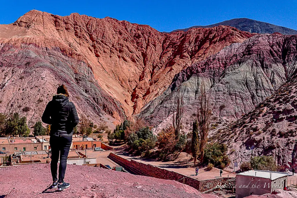 A woman in black stands on a hill in front of the Cerro de Siete Colores in Purmamarca. The landscapes are one of the reasons why Argentina is worth visiting