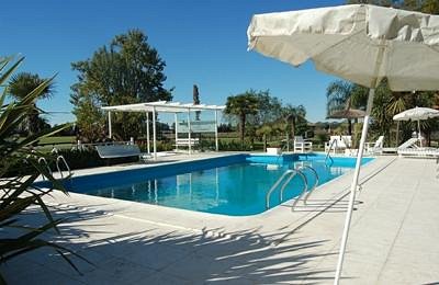 An outdoor swimming pool at Estancia Don Manuel with a white patio and sun loungers under umbrellas on a bright, sunny day.