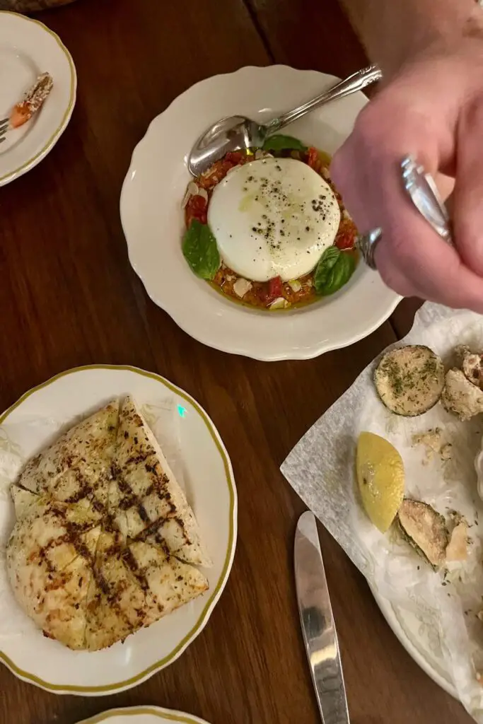 A beautifully plated burrata dish with roasted tomatoes and fresh basil at Via Triozzi in Lower Greenville, Dallas. The table also features slices of grilled focaccia and crispy fritto misto, showcasing the restaurant’s inviting and romantic Italian dining experience.