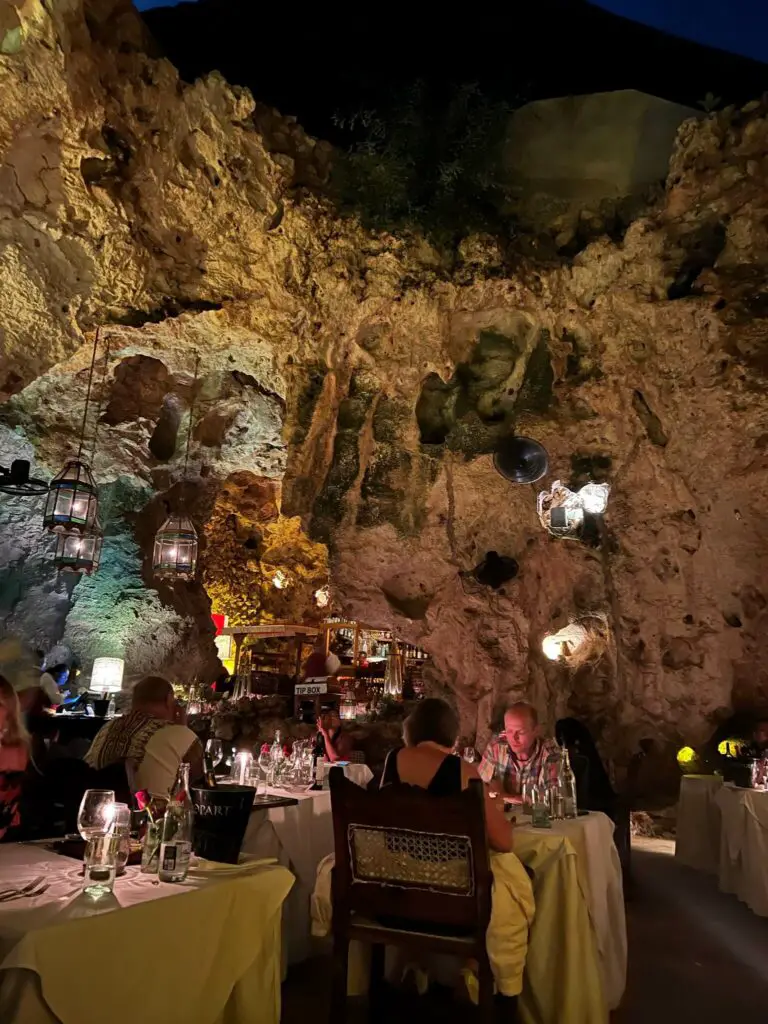 People eating inside a cave, there are tables with white tablecloths and lanterns hanging from the ceiling. This is Ali Barbours Cave Restaurant, a must-do when visiting Diani Beach in Kenya