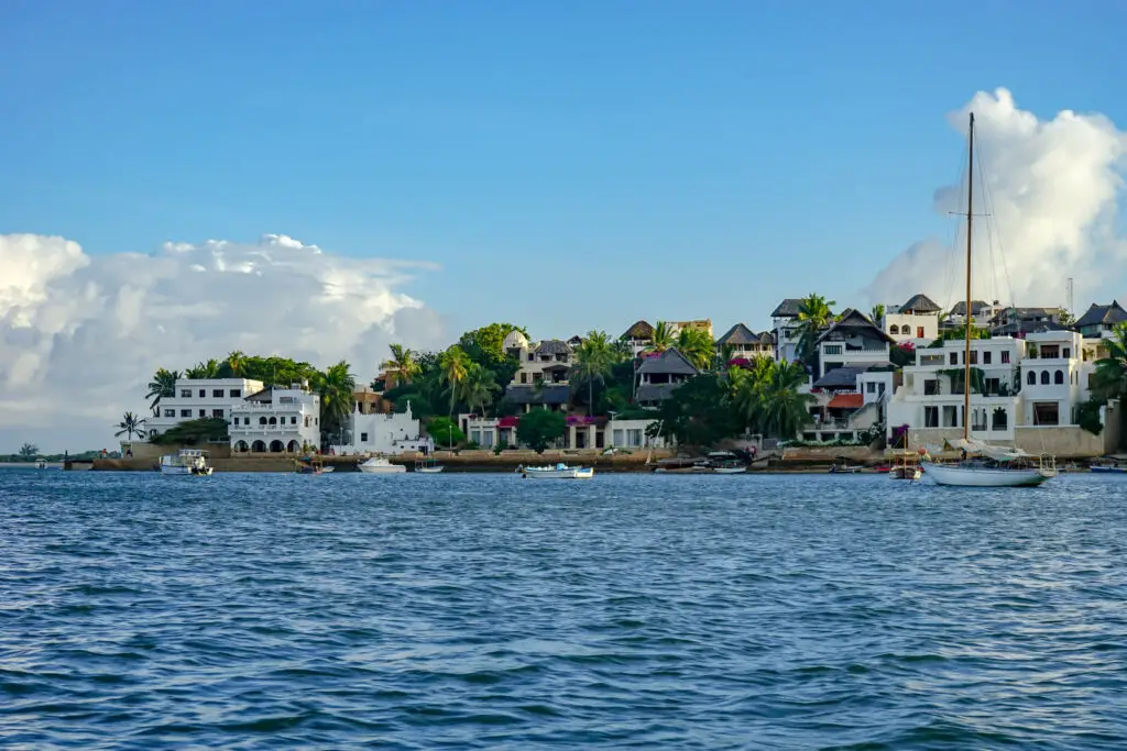 A view of Lamu in Kenya from the water - there are white buildings and green palm trees, with small boats on the water. Lamu is one of the best places to visit in Kenya for beach activities