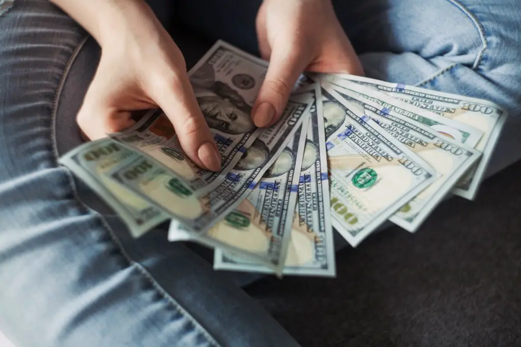 Two hands fan out several United States 100-dollar notes. The hands belong to someone wearing blue jeans. Exchanging money in Argentina can be tricky but can lead to good value if you know what to do.