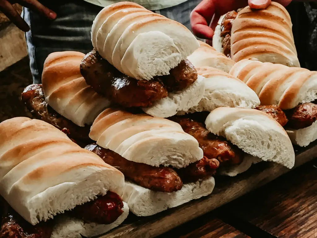 A tray of choripan, where the sausages are nestled in sliced white buns, held by someone in a casual setting, ready to be served. Choripan is the best street food in Argentina.