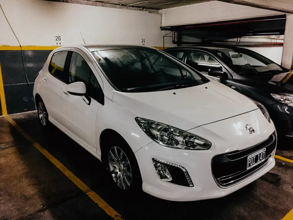 A white Peugeot is parked inside an underground car park next to a dark coloured car.
