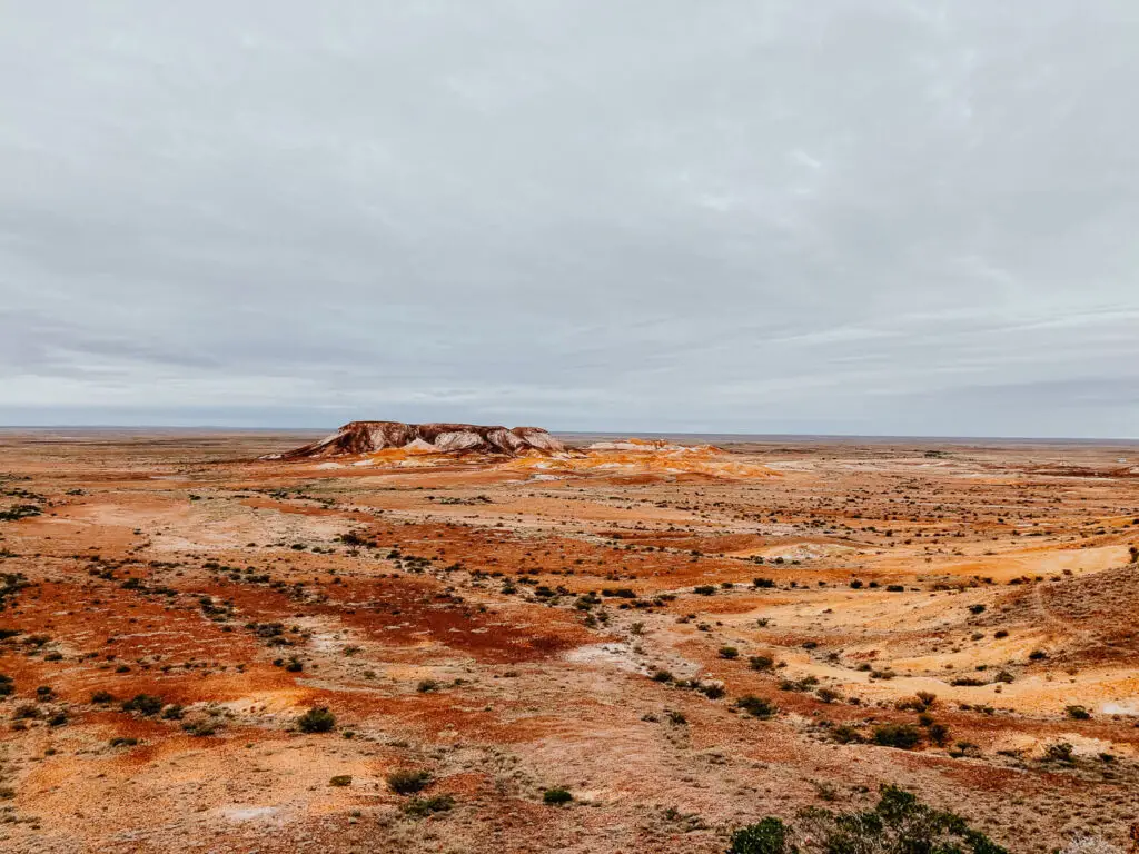 Landscape view of the Kanku-Breakaways Conservation Park in Coober Pedy, South Australia, a key attraction in Coober Pedy. Shows a red and orange landscape with mountains in the distance and a cloudy sky