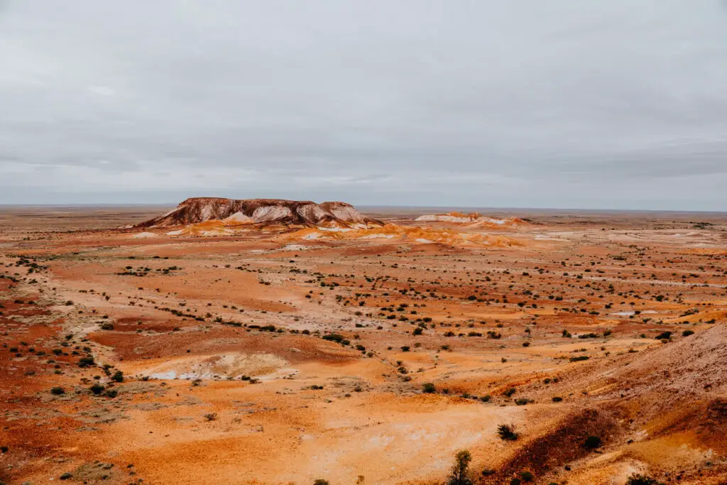 Landscape view of the Kanku-Breakaways Conservation Park in Coober Pedy, South Australia, a key attraction in Coober Pedy. Shows a red and orange landscape with mountains in the distance and a cloudy sky