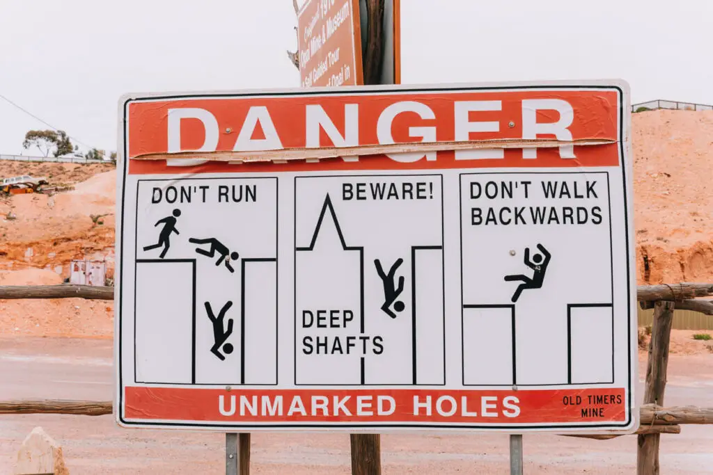 A red and white sign shows the dangers of unmarked mineshafts in Coober Pedy, with instructions not to run or walk backwards.