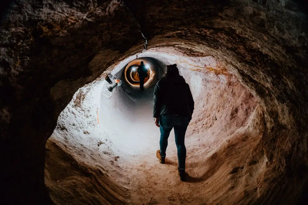 A woman in black walks hunched over to avoid hitting her head in a mineshaft in Coober Pedy