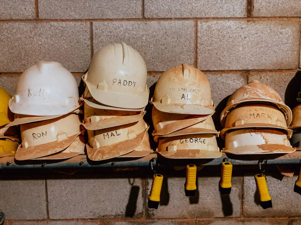 Dirty hard hats are stacked up on a shelf. The hard hats have handwritten names on the front. Mining is one of the key tourist attractions in Coober Pedy, South Australia