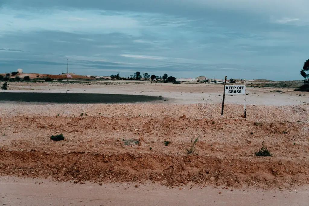 A sign says "keep off the grass" in front of the grassless golf course in Coober Pedy