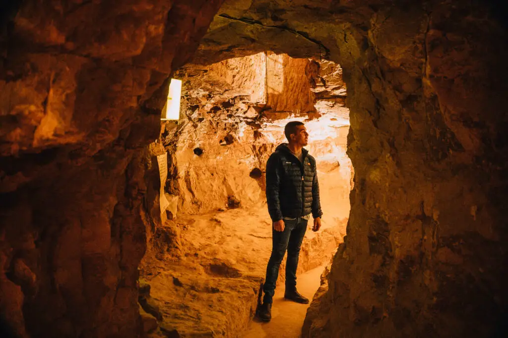 A man in black is silhouetted in one of the holes in the Old Timers Mine, the light is glowing a warm orange