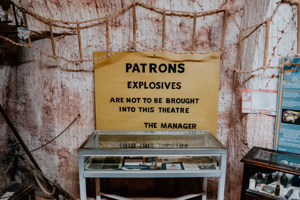 A sign behind a glass display case warns patrons not to bring explosives into the theatre. The sign is in Coober Pedy in the Old Timers Mine, one of the must-visit places to see in Coober Pedy.