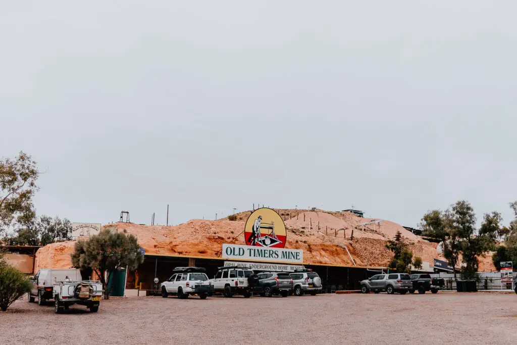 Old Timers Mine sign showing the location of the mine - one of the best things to do in Coober Pedy - which is built into a hill. Cars are parked out the front of the mine.