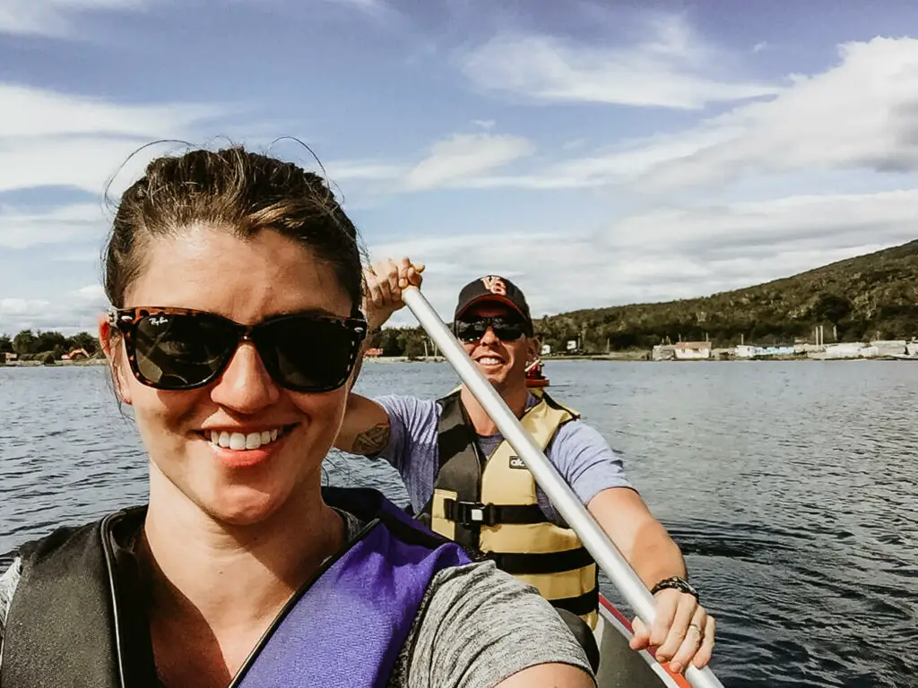 A woman (the author of this article) and man, both wearing life jackets, smile at a camera as they kayak through a lake in Ushuaia, Argentina.