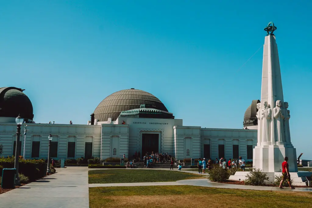 A view of the front of the Griffith Observatory, a low white building with domed roofs in Los Angeles, California