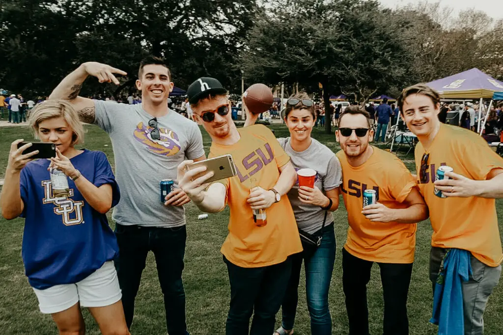 Two women and four men smile and pose at the camera, all are wearing LSU t-shirts at a tailgating party