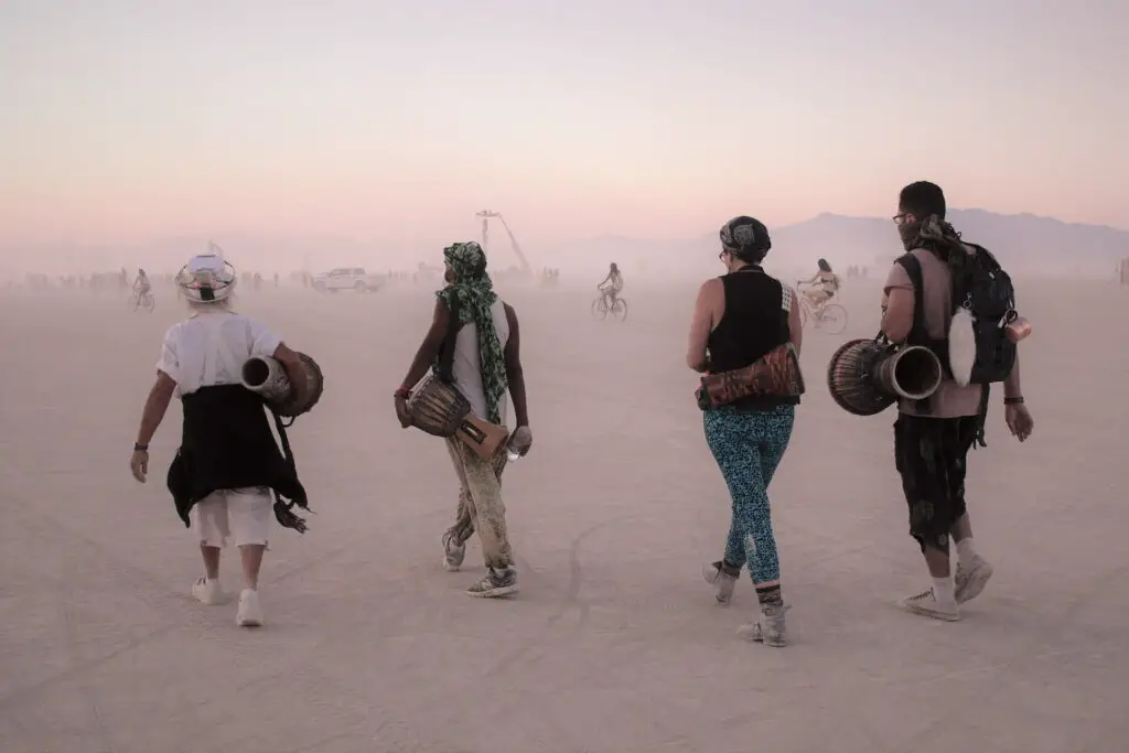 Four people with their backs to the camera walk into a dusty Burning Man Festival