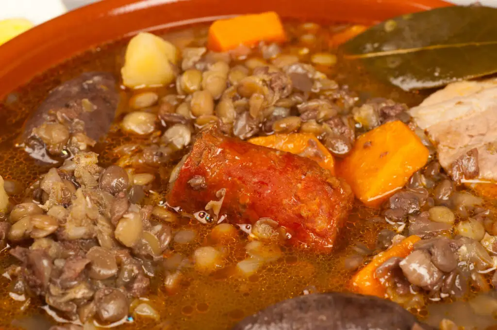 Stew in a clay pot. The image shows a close-up of a hearty stew with lentils, chunks of meat, carrots, and potatoes in a terracotta bowl.