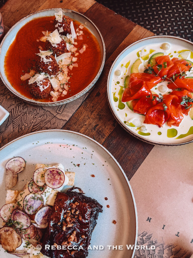 A table filled with beautifully plated dishes, including a rich meat entrée, meatballs in sauce, and a fresh seafood dish, represents contemporary Chilean cuisine—perfect for food-focused stops in a Santiago itinerary or a memorable meal during 2 days in Santiago.