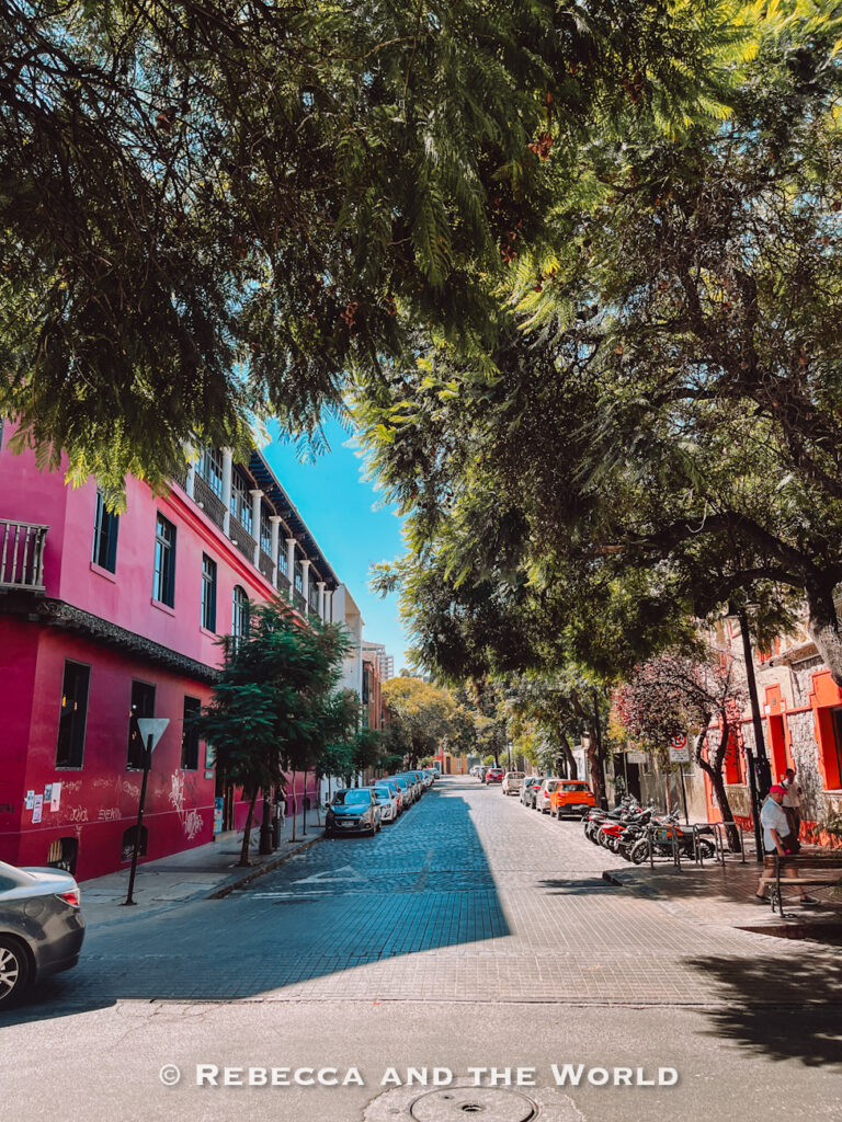 A tree-lined cobblestone street in Lastarria features colorful historic buildings, parked cars, and dappled sunlight—capturing the neighborhood’s charm and making it a great addition to a 2 days in Santiago itinerary for those exploring beyond the city center.