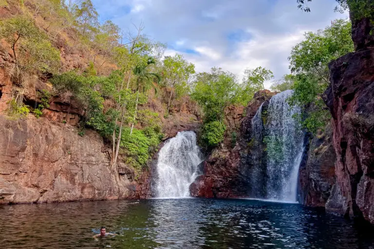 A man - the author's husband - swims in a natural pool at the base of Florence Falls in Litchfield National Park, surrounded by steep rock faces with vegetation.