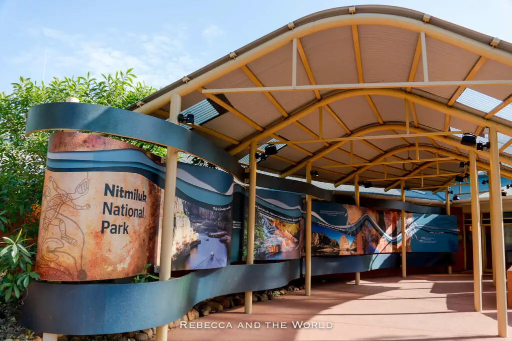 Entrance to Nitmiluk National Park Visitor Centre featuring an informative display with images and text, sheltered by a curved, modern metal roof.
