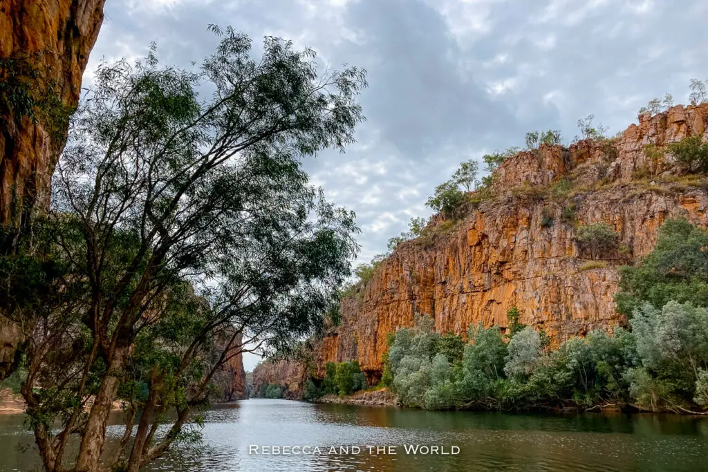 The Katherine River at the Second Gorge in Nitmiluk National Park - the scene shows a serene river flanked by steep rocky cliffs and green foliage, with a cloudy sky overhead.