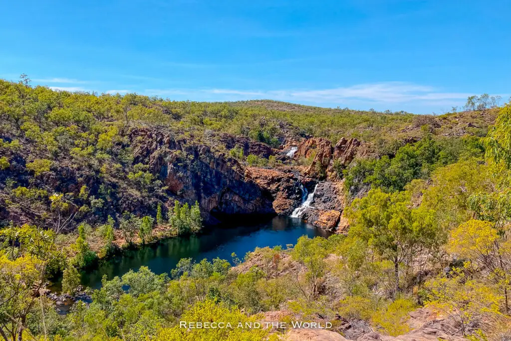 An elevated view of a Leliyn (Edith Falls) in Nitmiluk National Park, with a deep blue waterway running through the gorge, framed by steep, rocky cliffs and lush greenery. Two waterfalls can be seen in the distance.