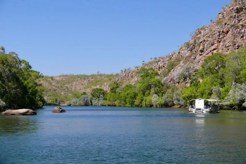 View of Nitmiluk GOrge from the water, showing the Katherine River surrounded by rocky gorge walls and a cruise boat heading along the water.