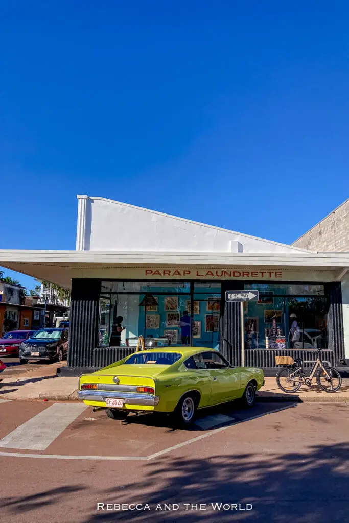 A bright green vintage car parked in front of a laundromat with a clear blue sky above. The car stands out against the modern cars in the background and the white building of the laundromat. Laundry Gallery is one of the coolest places to visit in Darwin.