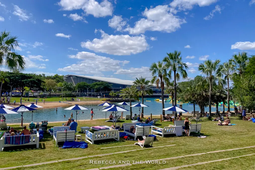 A sunny day at a recreational water park with a large inflatable obstacle course. People are lounging on the grass, and palm trees enhance the tropical setting. Visit the Darwin Waterfront Precinct when you're in Darwin.