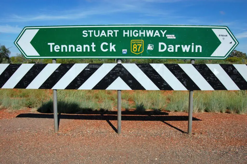 Road sign on the Stuart Highway pointing left to Tennant Creek and right to Darwin, against a backdrop of the red outback terrain.
