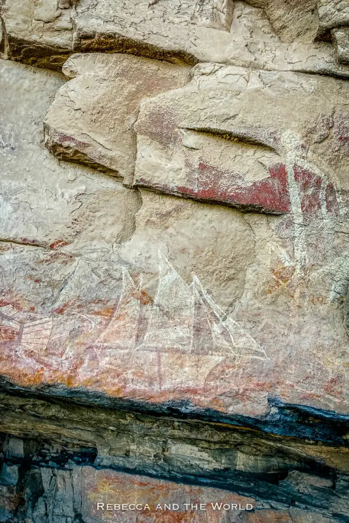 Close-up of ancient indigenous rock art in Kakadu National Park, with red ochre paintings depicting traditional figures and symbols on a stone wall. This is the ship in the Nanguluwurr art gallery.