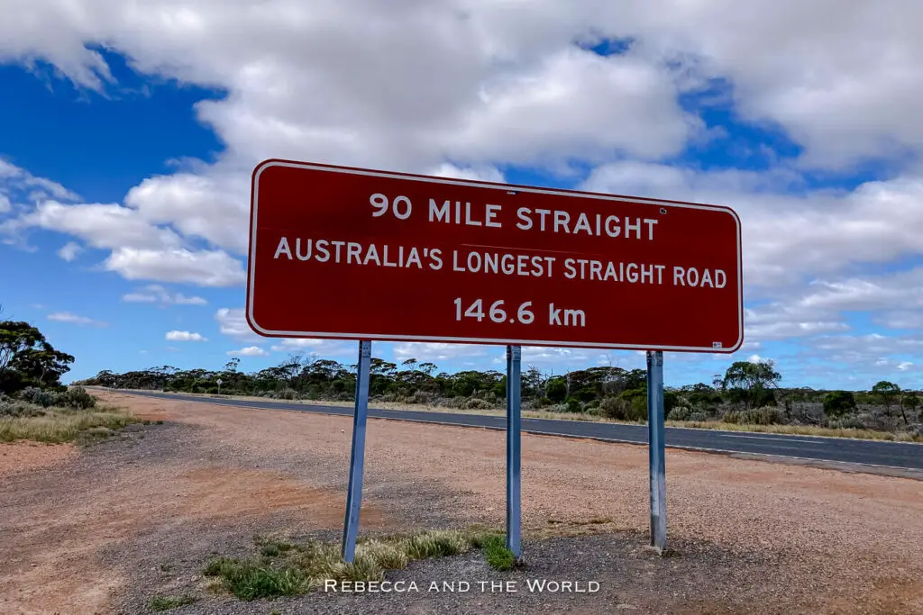 Road sign for the '90 Mile Straight,' which indicates it's Australia's longest straight road, set against a barren landscape with sparse vegetation. If you love driving, the Nullarbor should be on your Australian bucket list.