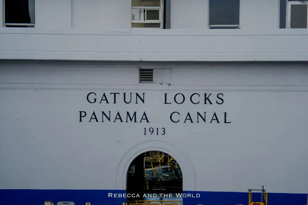 Close-up of the white wall of a canal lock with 'GATUN LOCKS PANAMA CANAL 1913' inscribed in black letters, with a small window showing inner workings.