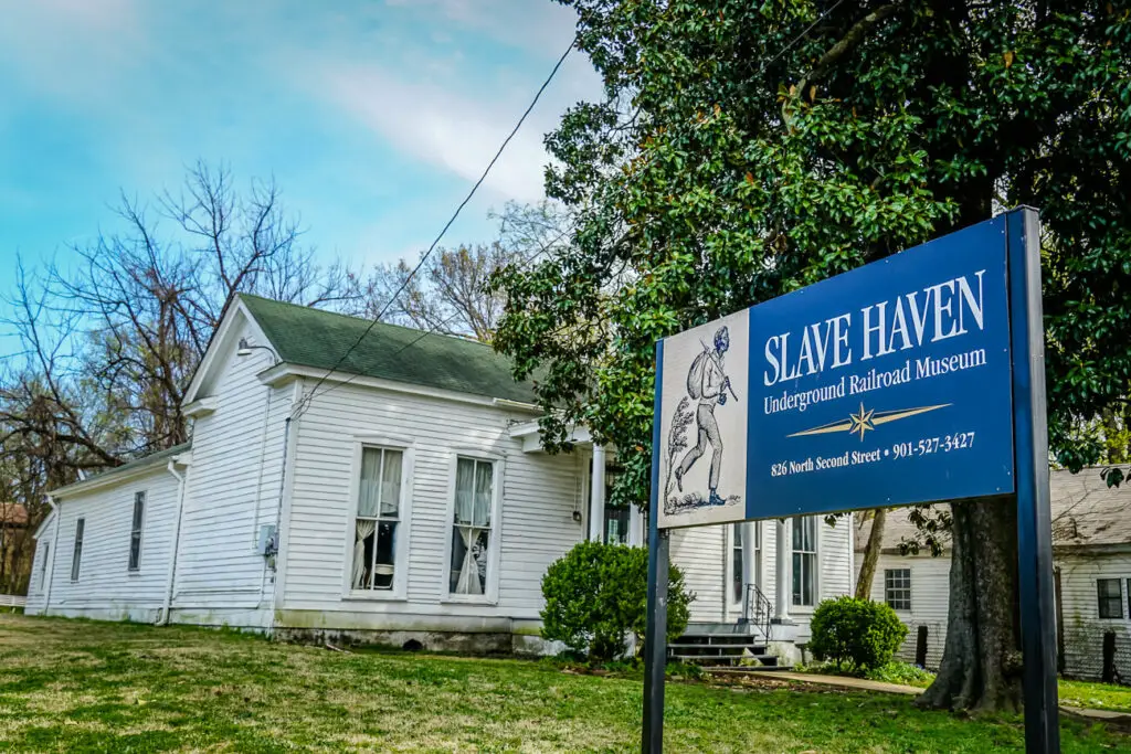 Exterior of the 'Slave Haven Underground Railroad Museum' in Memphis, Tennessee, with a sign in front, in a residential area, illustrating a historical white clapboard house.