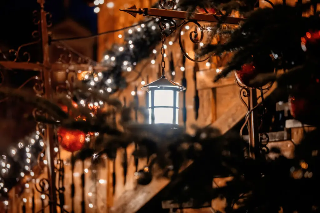 A warmly lit lantern hangs in focus, surrounded by festive lights and decorations, suggesting Fredericksburg's holiday atmosphere. One of the best times to visit Fredericksburg TX is during Christmas when the Christmas lights are put on and the streets are decorated.