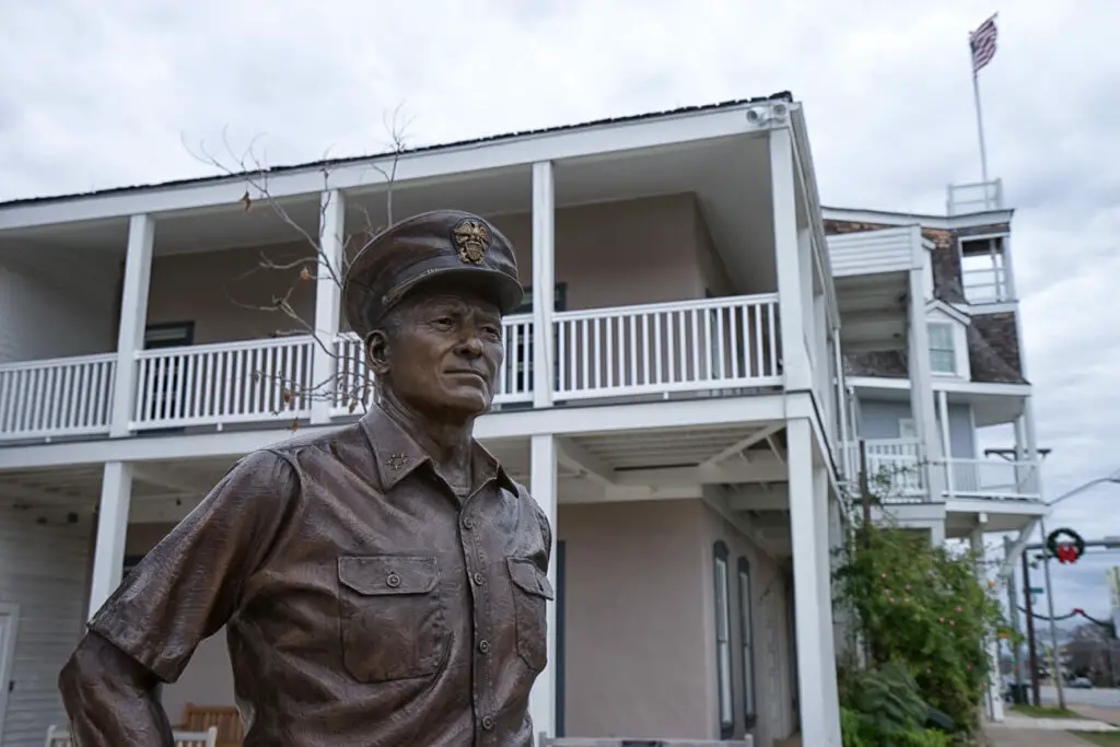 Bronze statue of a military figure in uniform in the foreground with a historic two-story building with American flag in the background. Visiting the National Museum of the Pacific War is one of the most fascinating things to do in Fredericksburg TX.