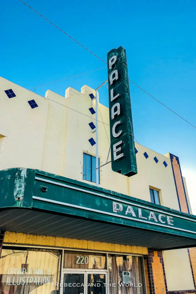 The facade of the Palace Theater building in Marfa with a vintage green vertical sign that says "PALACE", against a clear blue sky. One of the best things to do in Marfa Texas in a weekend is wander the streets to check out the art deco architecture.