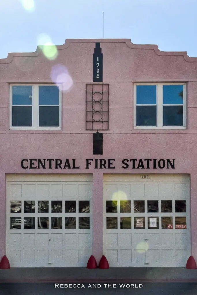 The 'CENTRAL FIRE STATION' building in Marfa, Texas, with a pale pink facade, dated 1938, and white garage doors, under the glare of sunlight reflecting off the camera lens. One of the best things to do in Marfa Texas in a weekend is wander the streets to check out the art deco architecture.